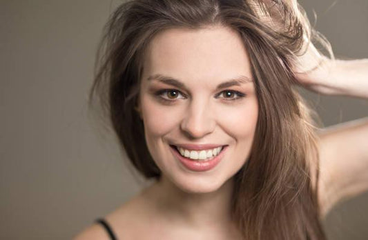 Smiling woman with healthy, voluminous hair, hand in hair, natural background